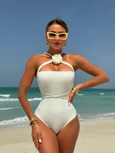 White one-piece halter bikini with 3D floral accent and criss-cross waist ties on the beach