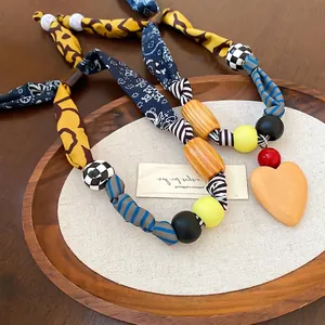 Collier artisanal en perles de tissu bohème avec pendentif cœur sur plateau bois