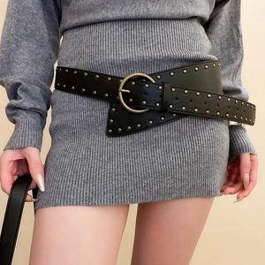 Close-up of black leather rivet belt with gold studs and round buckle on a grey dress