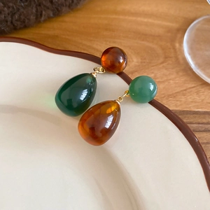 Detail of asymmetric resin teardrop earrings in amber and dark green with gold accents