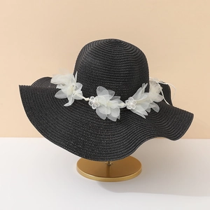 Détail d'un chapeau de paille noir avec fleurs 3D blanches et perles sur support doré