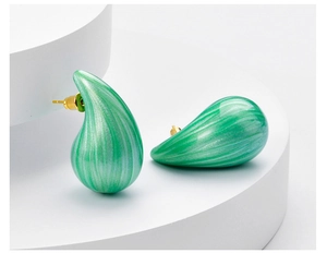 Detail of emerald green teardrop earrings with marble texture on white geometric stand
