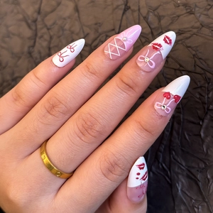 Macro shot of pink and white almond nails with red bows, cherries, and rhinestones