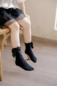 Detail shot of black knitted baby socks featuring large satin bows and ruffled edges