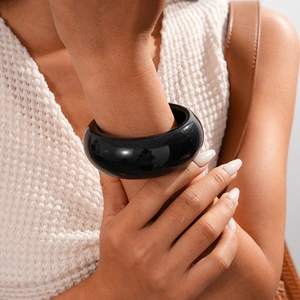 Close-up of a wide black resin bangle featuring a glossy finish on a female wrist