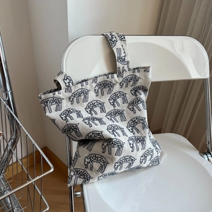 Close-up of cream canvas tote bag with black animal embroidery hanging on a chair