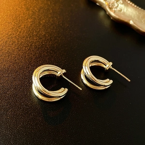 Close-up of golden multi-layer C-shaped metal hoop earrings on black texture