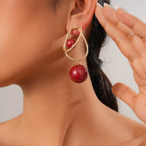 Detail shot of a golden metal drop earring with two red spherical beads on a female model