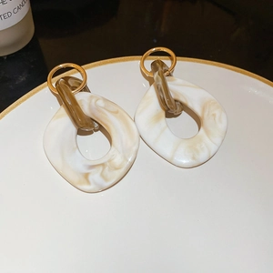 Macro detail of marble resin hoop earrings with gold metal rings on a white plate