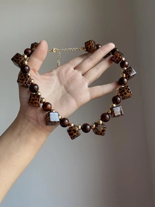 Close-up of leopard resin blocks, brown wooden beads, and gold metal beads necklace detail
