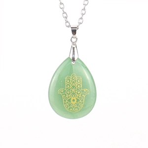 Macro detail of green crystal drop pendant with golden Hamsa Hand on a silver chain