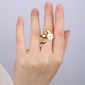 Détail d'une bague fleur en or 18k avec fleur en nacre et perle sur un doigt féminin