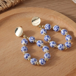 Blue and white porcelain beaded drop earrings with golden circular studs on wood
