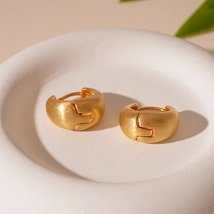 Close-up of matte gold geometric earrings with a brushed metal texture on a ceramic tray