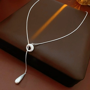 Detailed view of silver water drop pendant on a sleek snake chain necklace over leather