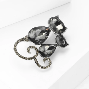 Close-up of a stylish cat brooch made with dark metal and faceted gemstones on white podium