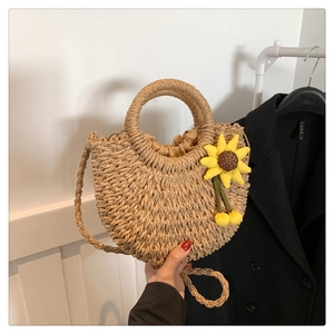Details einer Stroh-Umhängetasche mit Sonnenblumen-Anhänger und geflochtenem Riemen