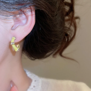 Close-up of bamboo-style gold C-shape earrings with yellow enamel and inlaid zircons