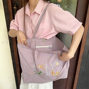 Détail du sac en toile lilas avec broderie arc-en-ciel et poche frontale zippée