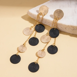 Close-up of gold and black textured metal discs on elegant long tassel earrings