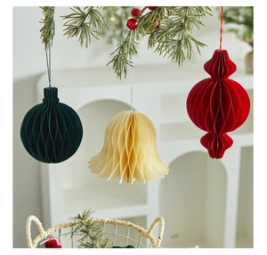Close-up of honeycomb paper Christmas ornaments in bell and sphere shapes hanging on a pine branch