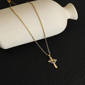 Detail of gold heart cross pendant necklace with zircon stones on white ceramic vase