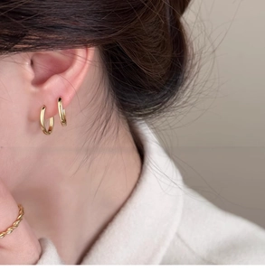 Dettaglio di orecchini a cerchio ovali placcati oro 18k indossati in doppio piercing