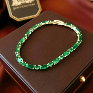 Detailed macro of gold plated tennis bracelet featuring emerald green square zircons