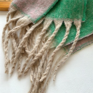 Macro shot of green and pink plaid pattern with beige tassels on soft wool scarf