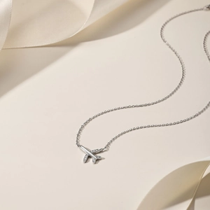 Detailed view of silver airplane pendant with sparkling zircon wings on silk fabric