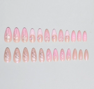 Vue détaillée d'ongles amande à presser avec nœuds 3D, perles et dégradé de rose
