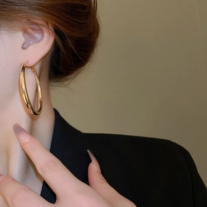 Detailed view of large polished golden hoop earrings worn with elegant black blazer styling
