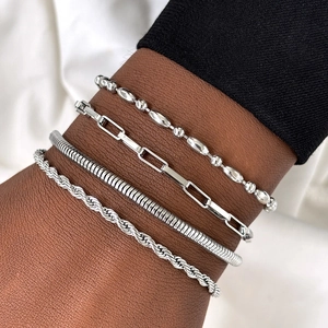 Close-up of four silver-toned minimalist chains layered on wrist including snake and rope link