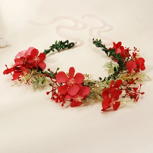 Close-up of a floral wreath headband featuring red faux flowers and pink ribbon ties