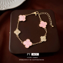 Macro detail of gold four-leaf clover bracelet with pink marble inlay and crystals