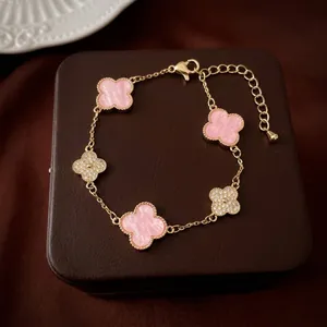 Macro detail of gold four-leaf clover bracelet with pink marble inlay and crystals
