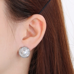 Detail of round silver stud earring with central pearl and halo of crystal accents
