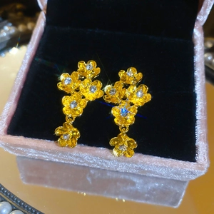 Close-up of golden zircon flower drop earrings on a pink velvet jewelry box