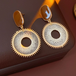 Detail of gold round earrings featuring white woven mesh pattern and brown oval resin accent