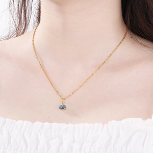 Detail of a minimalist gold stainless steel necklace with blue cherry pendant on a model