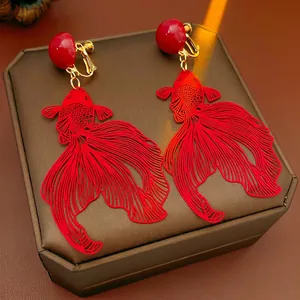 Boucles d'oreilles clips poisson rouge évidées avec spirales dorées sur boîte à bijoux