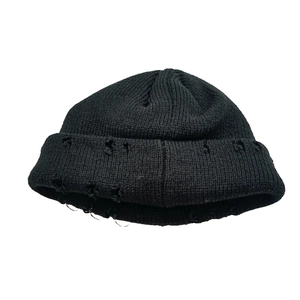 Détail du bonnet en maille noire avec anneaux métalliques et finitions déchirées