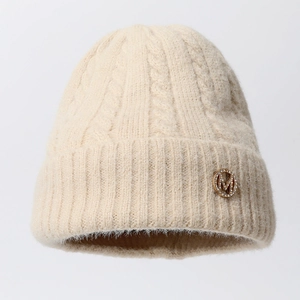 Close-up of beige cable knit beanie featuring a gold rhinestone M metal emblem