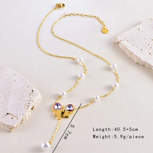 Détail du collier de perles noeud doré avec cristaux coeur violets et pompon sur pierre