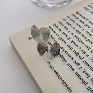 Detail of silver fan-shaped earrings with pleats on a minimalist book background