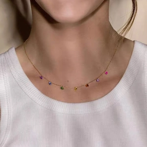 Detailed view of a gold station necklace with rainbow colored gemstones on a model