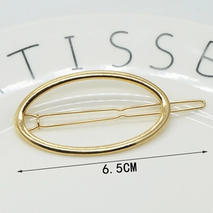 Macro shot of a 6.5CM golden oval hollow alloy hair clip on a white ceramic plate