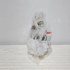 Close-up of a glowing snowman plush with a green knit hat in clear protective packaging