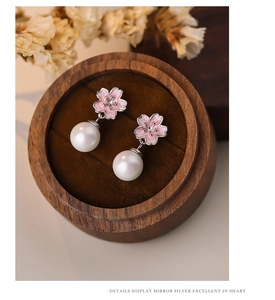 Close-up of pink cherry blossom pearl earrings in a wooden box with soft lighting
