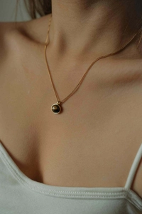 Close-up of a 18K gold chain necklace with a round brown tiger eye stone on a model